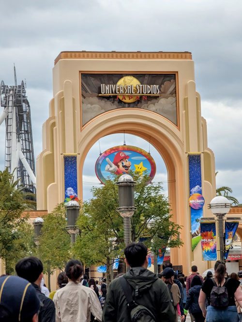Arco de entrada de Universal Studios Japan con el globo de Mario al fondo y visitantes esperando para entrar.