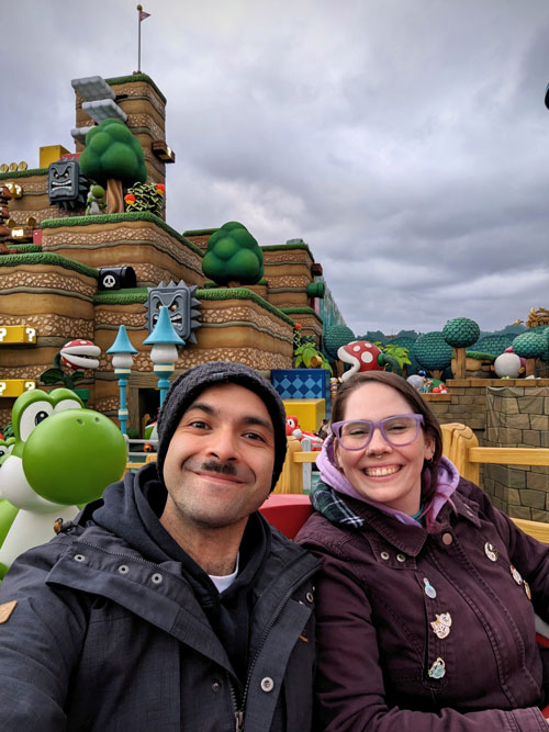 Pablo, autor de Vamos Pa' Japón, y su esposa haciéndose una selfie en Super Nintendo World, con Yoshi y los decorados del Reino Champiñón al fondo.