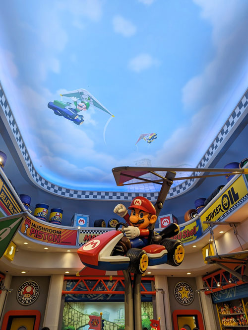 Figura de Mario en su kart bajo un techo pintado como un cielo, en una tienda de Mario de Universal Studios Japan.