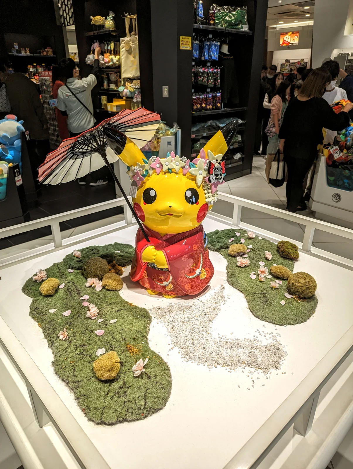 Estatua de Pikachu con kimono rojo y sombrilla japonesa sobre un jardín de musgo en el Pokémon Center Kyoto