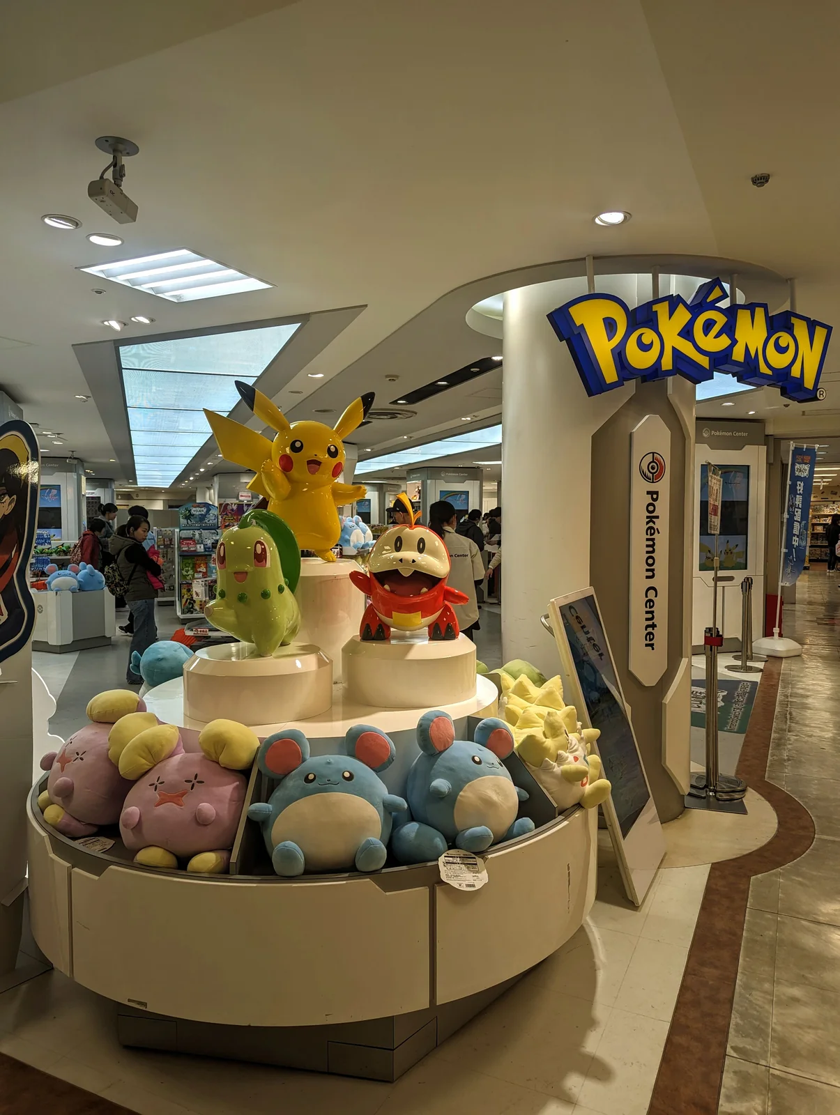 Pikachu, Chikorita y Fuecoco sobre peluches junto al letrero del Pokémon Center Nagoya, en Matsuzakaya