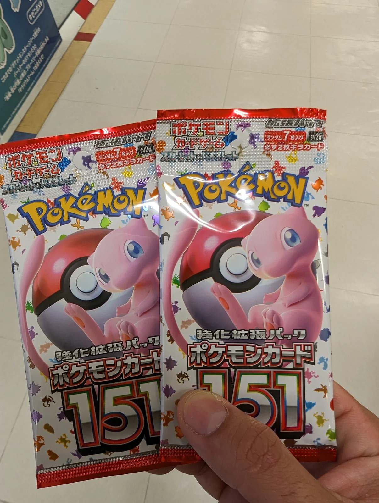 Dos sobres de cartas Pokémon de la colección 151 en la mano